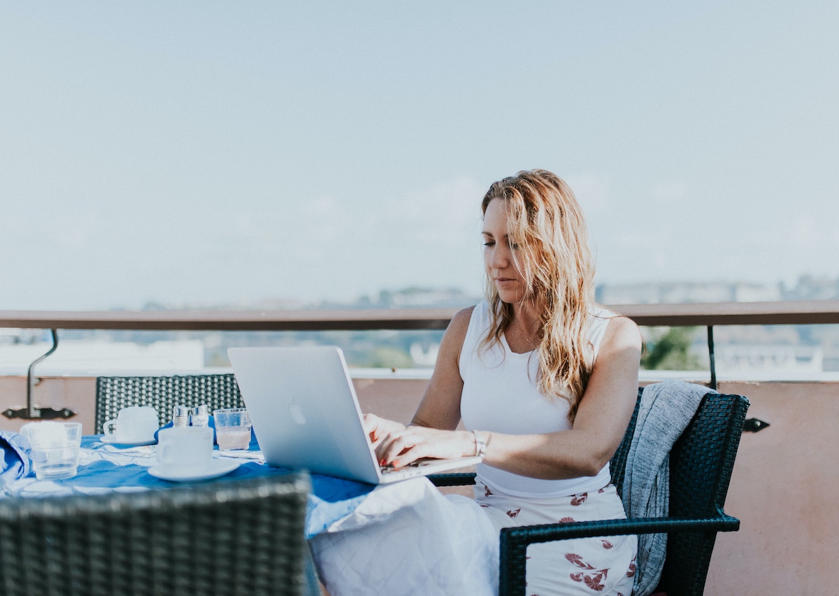 Overemployment: What It Is, How to Be Overemployed, and How It Can Accelerate Your Path to Financial Freedom - Woman working on laptop in a rooftop cafe - Frayed Passport