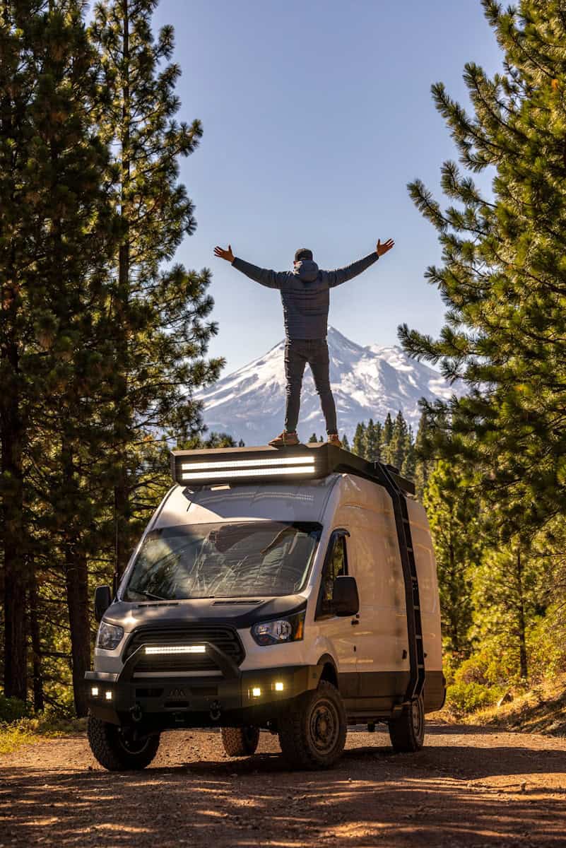 a man standing on top of a van in the woods