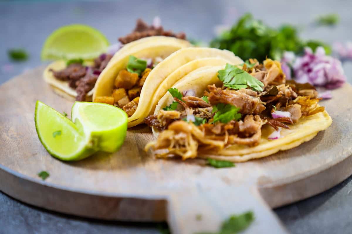 Photo by Frankie Lopez a wooden plate topped with three tacos and a lime