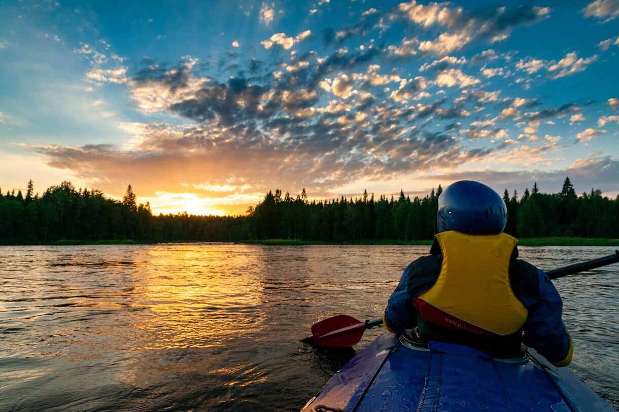 Coolcations: Travel to Stay Cool While Temps Rise - Frayed Passport - a person in a kayak on a lake with trees and a sunset