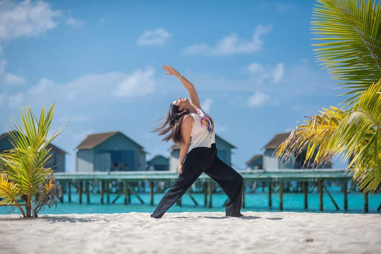 5 Types of Travel and How To Choose Which Works for You - Frayed Passport - Woman practicing yoga on a sandy beach by the ocean.